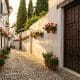 Callejón empedrado del Albaicín con macetas de geranios, portal de carmen y artesano de taracea