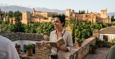 Guía historiadora con libreta y cámara frente a la panorámica de la Alhambra y Sierra Nevada