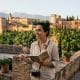 Guía historiadora con libreta y cámara frente a la panorámica de la Alhambra y Sierra Nevada